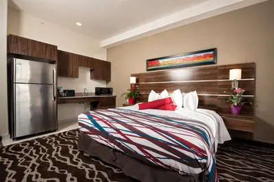a hotel room with a bed and a refrigerator at Encore Suites by Service Plus Inns in Grande Prairie