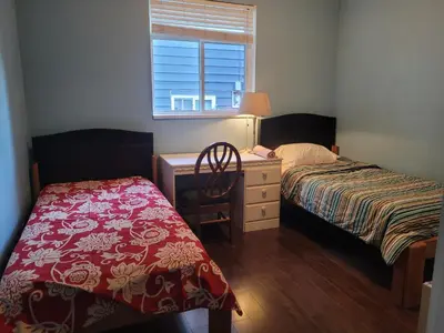 a bedroom with two beds and a desk and a window at Vancouver Jenny's Guesthouse in Coquitlam