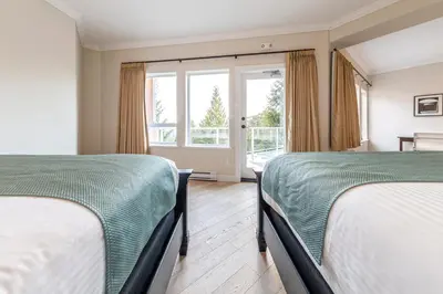 two beds in a room with a window at Villa Eyrie Resort in Malahat
