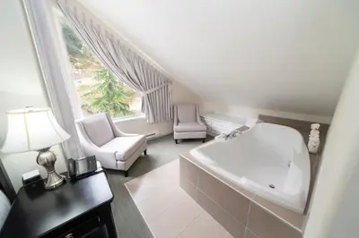 a white bathroom with a tub and a chair and a window at Villa Eyrie Resort in Malahat