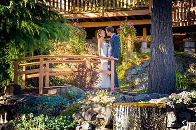a bride and groom standing on a bridge in a garden at Villa Eyrie Resort in Malahat