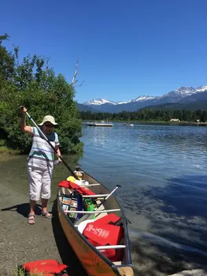 a man standing next to a boat on a lake at Mountainview 1 bedroom suite with check in services king size bed walk to Village WIFI cable TV free parking boot and glove warmer in Pemberton