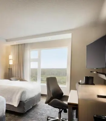 a hotel room with a bed and a chair and a window at Hotel Dene & Conference Centre in Cold Lake