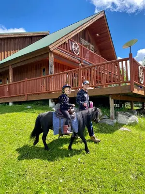 two people riding a horse in front of a cabin at Montana Hill Guest Ranch in Bridge Lake