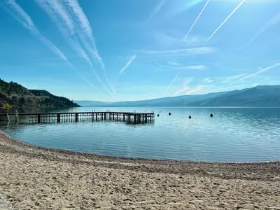 a beach with a pier and people in the water at Peachland Beach Resort in Peachland