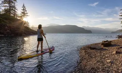 a woman standing on a paddle board in the water at Eleven Revelstoke Lodge in Revelstoke