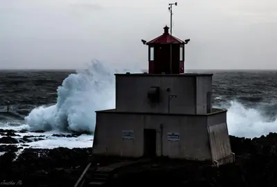 a lighthouse in the ocean with a wave behind it at Waterfront Timber-Frame Cottage! in Ucluelet