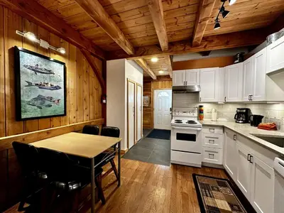 a kitchen with white cabinets and a table and a dining room at Waterfront Timber-Frame Cottage! in Ucluelet