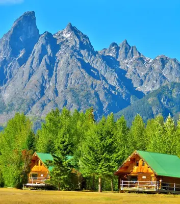 two wooden cabins with mountains in the background at Rocky Ridge Resort-BC in Smithers