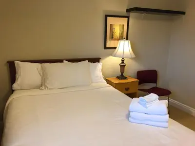 a bedroom with a white bed with a lamp and a chair at Cozy Bedrooms Guest House in Vancouver