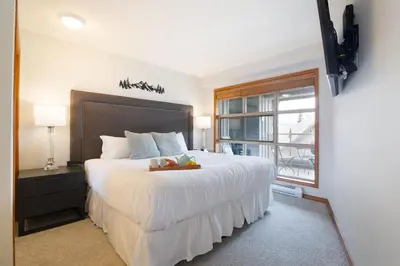 a bedroom with a large white bed with a window at Aspens Mountain Side Resort in Whistler