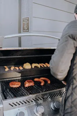 a person cooking hamburgers and hot dogs on a grill at Basecamp Resorts Canmore in Canmore