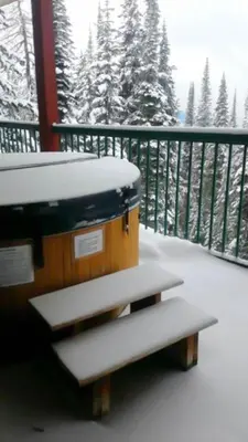 a snow covered bench on a balcony with a view of snow covered trees at Vacation Homes by The Bulldog- Berker's Suite A in Silver Star