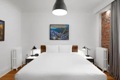 a bedroom with a large white bed and two tables with lamps at Victorian Hotel in Vancouver