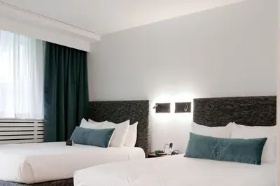 two beds in a hotel room with green curtains at The Burrard in Vancouver