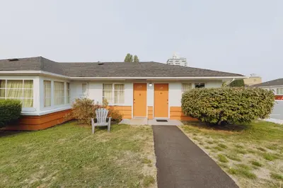 a white house with an orange door and a chair at 2400 Motel in Vancouver