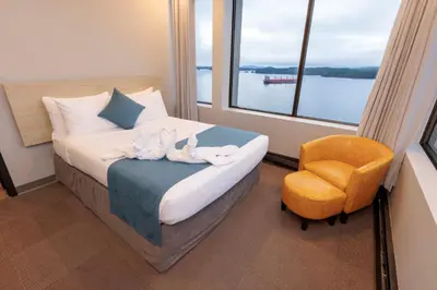 a bedroom with a bed and a chair and a window at Highliner Hotel in Prince Rupert