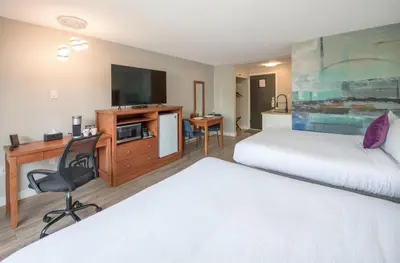 a hotel room with two beds and a desk and a television at Coast Metro Vancouver Hotel in Burnaby