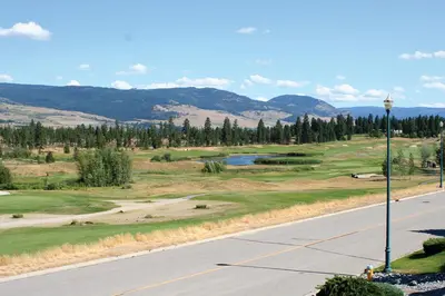 an empty road with a golf course and mountains in the background at Quail Ridge in Kelowna