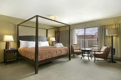a hotel room with a bed and a table and chairs at Ramada by Wyndham Kelowna Hotel & Conference Center in Kelowna