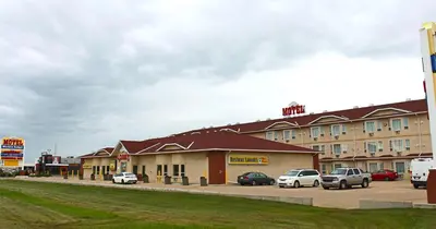 a large building with cars parked in a parking lot at Western Budget Motel Ponoka in Ponoka