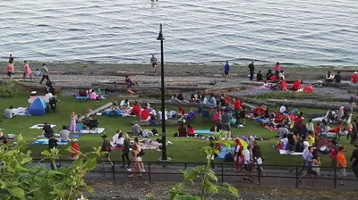 a group of people sitting on the grass by the water at White Rose House in White Rock
