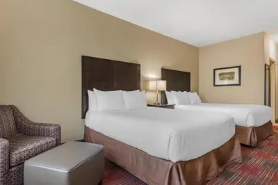 a hotel room with two beds and a chair at Best Western Plus Red Deer Inn & Suite in Red Deer