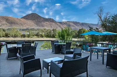 a patio with tables and chairs with mountains in the background at Riverland Inn & Suites in Kamloops