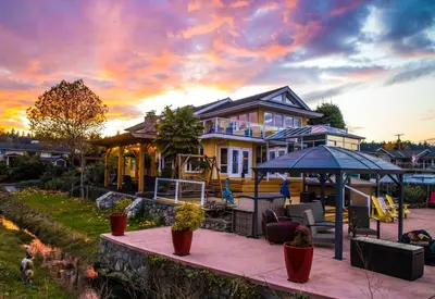 a large yellow house with a sunset in the background at Birds of a Feather Victoria Oceanfront Studio Suites in Colwood