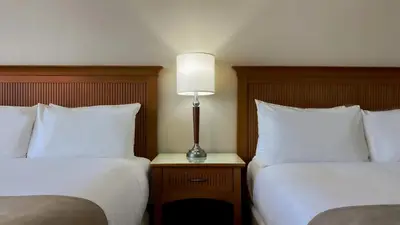 a hotel room with two beds and a lamp on a night stand at Coast Capri Hotel in Kelowna