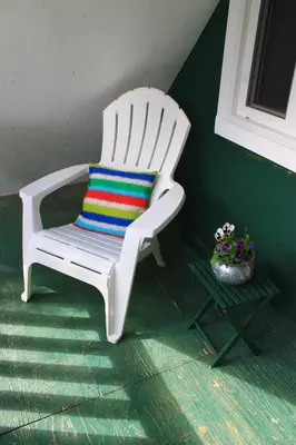 a white rocking chair with a colorful pillow and a table at Vines and Puppies Hideaway in Jade City