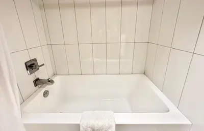 a white bath tub in a white tiled bathroom at Linda Vista Motel in Surrey