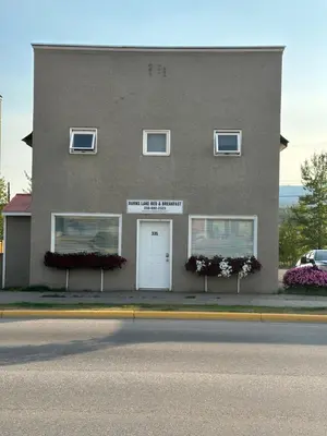 a gray building with a white door and three windows at Burns Lake Bed and Breakfast in Burns Lake