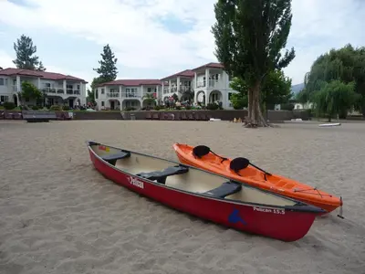 an orange kayak sitting on the sand in front of houses at Sandy Beach Suites in Osoyoos