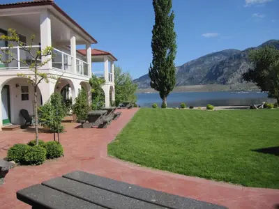 a house with a lawn and a lake in the background at Sandy Beach Suites in Osoyoos