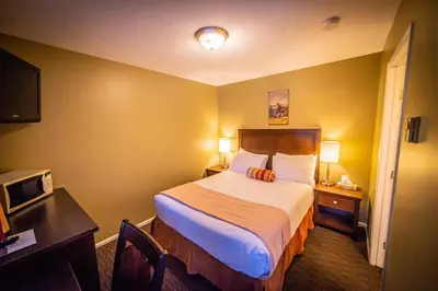 a small hotel room with a bed and a desk at Alpine Inn & Suites in Nelson