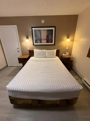 a large white bed in a room with two tables at Canadas Best Value Inn Kelowna in Kelowna