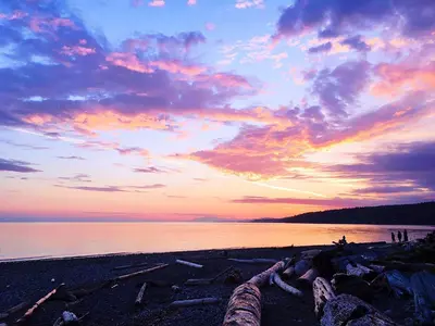 a sunset on a beach with people on the shore at Bonniebrook Lodge in Gibsons