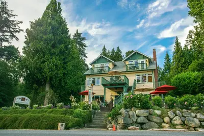 a large yellow house with a staircase leading up to it at Bonniebrook Lodge in Gibsons
