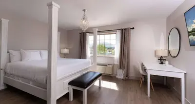 a white bedroom with a bed and a desk and a window at Prestige Rocky Mountain Resort Cranbrook, WorldHotels Crafted in Cranbrook
