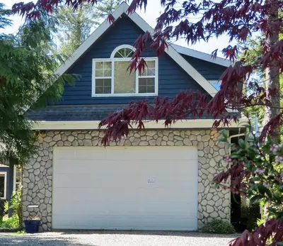 a blue house with a white garage door at Cobble Wood and Bird Sanctuary Guest Houses in Tofino