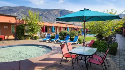 a table with chairs and an umbrella next to a pool at Sahara Courtyard Inn & Suites Osoyoos in Osoyoos
