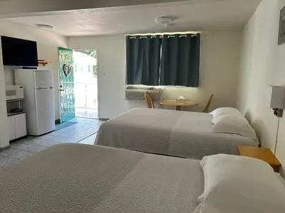 a bedroom with two beds and a table and a kitchen at Empire Motel in Penticton
