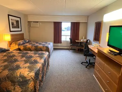 a hotel room with two beds and a desk with a television at BCMInns - Peace River in Peace River