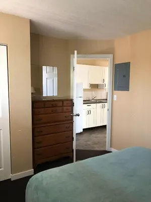 a bedroom with a bed and a dresser and a kitchen at Sun Beach Motel in Osoyoos