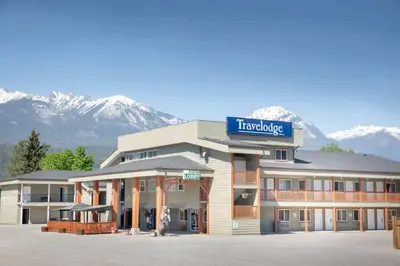 a hotel with snow covered mountains in the background at Travelodge by Wyndham Golden Sportsman Lodge in Golden