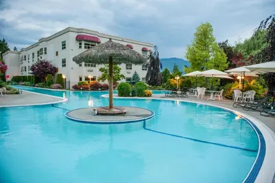 a large swimming pool with an umbrella in front of a building at Hilltop Inn - Salmon Arm in Salmon Arm