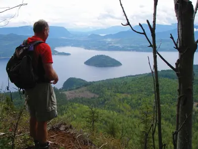 a man with a backpack standing on a hill overlooking a lake at Hilltop Inn - Salmon Arm in Salmon Arm