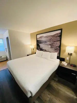 a hotel room with a large bed with white sheets at Super 8 by Wyndham 100 Mile House in One Hundred Mile House