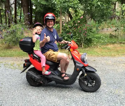 a man and a little girl sitting on a scooter at Sticks and Stones Cottage-Arbutus Grove in Galiano
